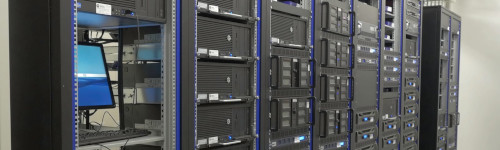 Rows of black server racks with blue indicator lights in a data center illustrate the concept of what is virtualization; one open rack reveals a computer monitor and keyboard.
