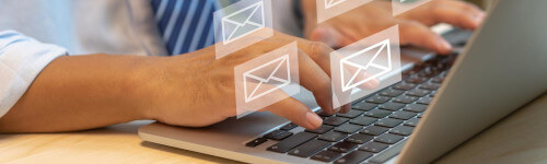 Person typing on a laptop keyboard with illustrated email icons floating above, suggesting email hosting or sending messages seamlessly.
