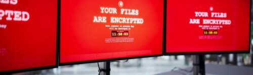 Three computer monitors display a red ransomware message reading "Your files are encrypted" with a countdown timer and payment instructions.