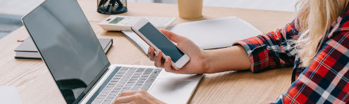 A woman is using a laptop and cell phone while sitting at a desk.