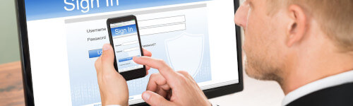 A person enters login credentials on a smartphone while a computer screen displays a sign-in page in the background, emphasizing the importance of email security.