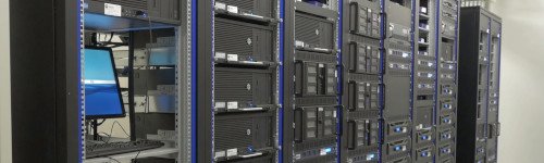 Rows of black server racks with blue indicator lights in a data center illustrate the concept of what is virtualization; one open rack reveals a computer monitor and keyboard.
